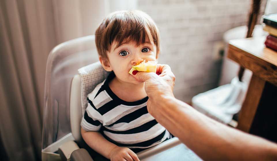 the baby is sitting in a highchair and being fed pineapple by his mom